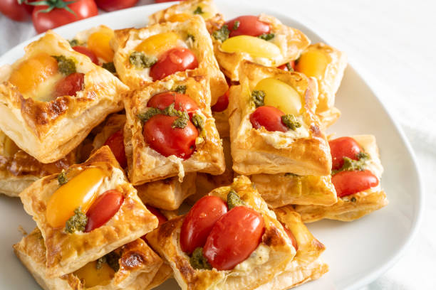 Puff pastry snacks with tomato, cream cheese and herb pesto, finger food on a white plate for a cold party buffet, selected focus