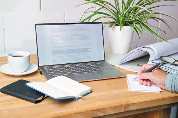 istock Hand writing notes on a wooden desk with laptop, notebooks, file folder and coffee cup, office workplace at home, copy space, selected focus 1607350531