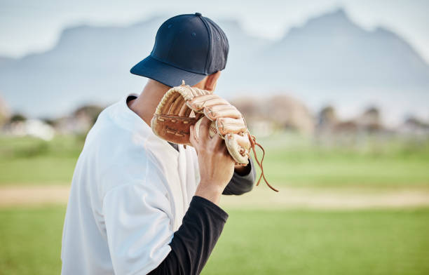 istock Pitcher, back view or baseball player training for a sports game on outdoor field stadium. Fitness, young softball athlete or focused man pitching or throwing a ball with glove in workout or exercise 1607356973