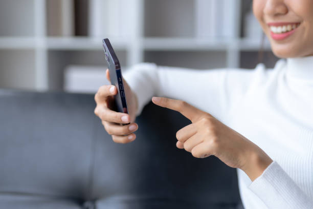 istock Beautiful young smiling Asian woman using smartphone on sofa at home. 1607362029