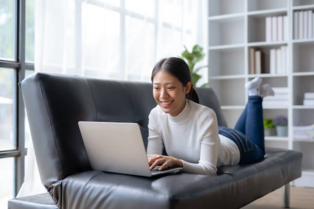 istock Happy young Asian woman relaxing using laptop computer on sofa at home. 1607363184