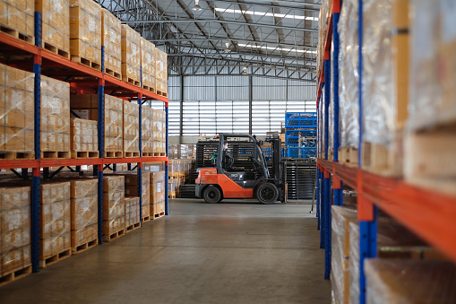 Interior of modern warehouse of auto parts factory with forklift trucks parked near shelves.