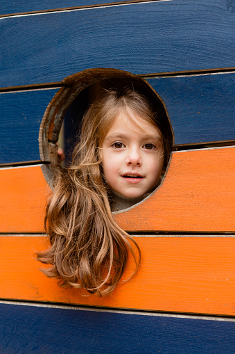 Cheerful little girl peeking from a hole in the playground