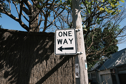 One way street sign on a wooden utility pole with a fence and blue sky behind.
