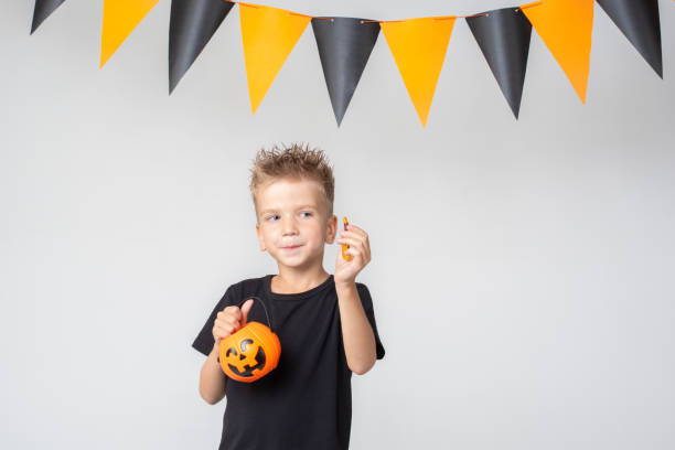 istock A happy smiling little boy holds a pumpkin-shaped Halloween basket and eats candy, marmalade on a white 1607381996