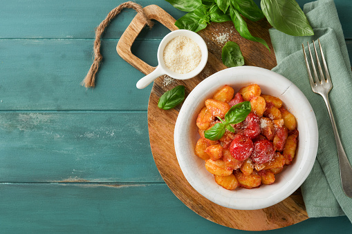 Potato gnocchi. Traditional homemade potato gnocchi with tomato sauce, basil and parmesan cheese on turquoise rustic kitchen table background. Traditional Italian food. Top view.