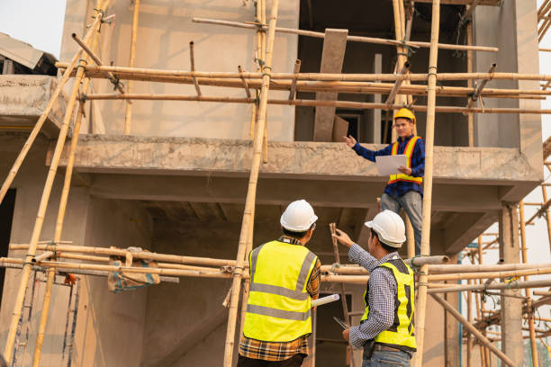 istock Architects and engineers working together sketching building plans and discussing at construction site wearing uniforms and helmets standing on construction site about large industrial architecture. 1607388910
