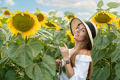 A beautiful and happy girl, in a straw hat, stands in a field with yellow sunflowers against the blue sky. Peace concept. Symbol of Ukraine. Close-up.
