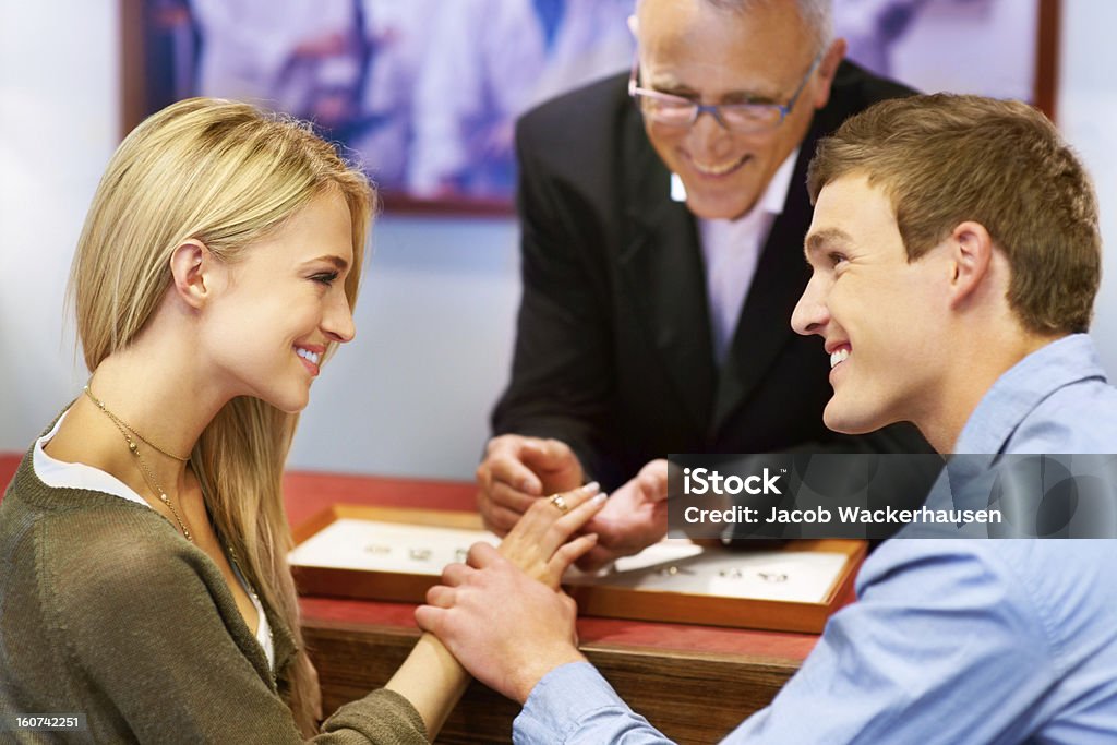 This ring will signify our eternal love Lovely couple looking at each other while a jeweler helps them try on engagement rings Shopping Stock Photo
