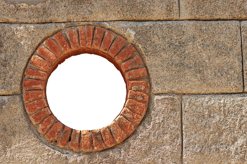 Close-up of a small round window with brick frame isolated on white background with copy space. La Spezia province, Liguria, Italy, Europe.