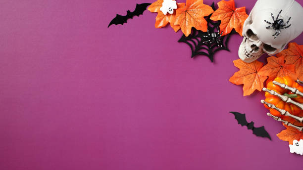istock Halloween scary decorations on purple background. Halloween banner template with skull, spiders webs, bats, skeleton hands, ghosts, maple leaves. Flat lay, top view. 1607442648