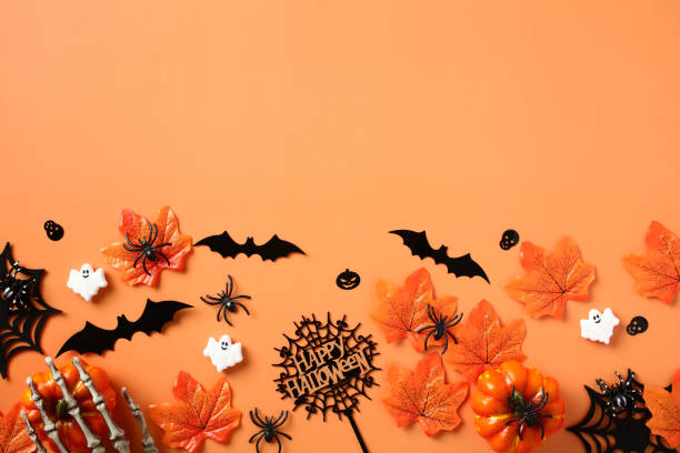 istock Halloween flat lay composition with pumpkins, skeleton hands, spiders, bats, maple leaves on orange background. Happy Halloween banner design. 1607450290