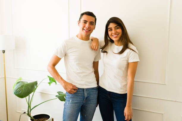 istock Cheerful couple at home using white t-shirts with a mockup design 1607473891
