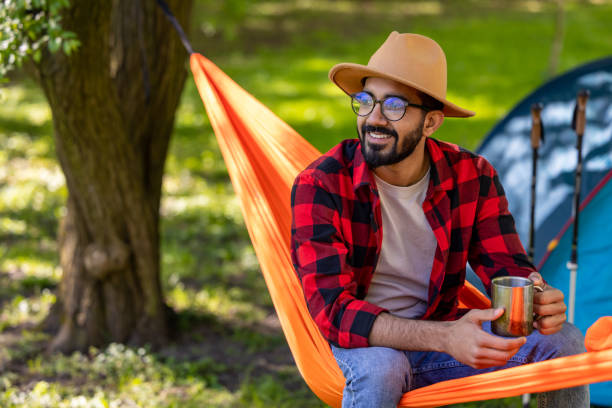 istock Smiling man with cup in hands enjoying nature in a hammock 1607474987