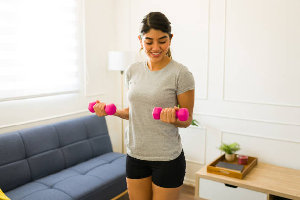 istock Happy active woman lifting weights at home 1607479928