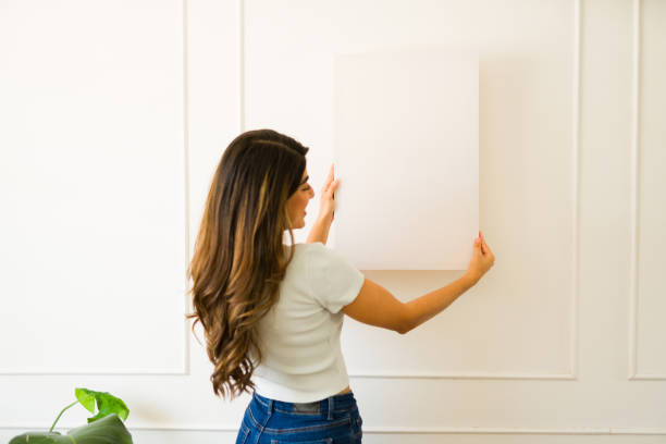 istock Attractive young woman hanging a blank picture 1607484312