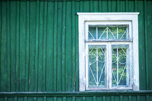 A window of an old country house with wooden shutters and flowers behind the glass
