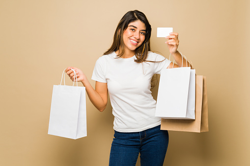 Happy beautiful young woman going shopping with a credit card wearing a mock-up t-shirt and blank shopping bags