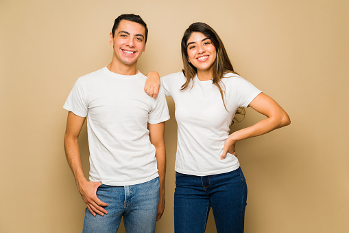 Happy attractive couple smiling while wearing white matching mock-up t-shirts against a studio background