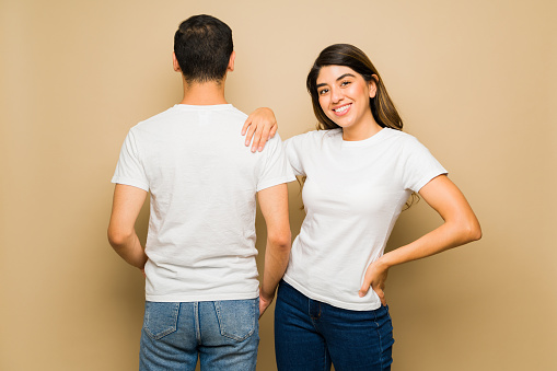 Attractive woman and man showing the front and back of a white matching mock-up t-shirts against a studio background