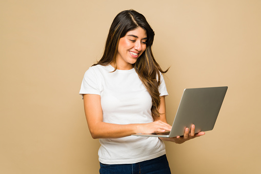 Happy beautiful woman smiling wearing a white mockup t-shirt using a laptop in a studio background