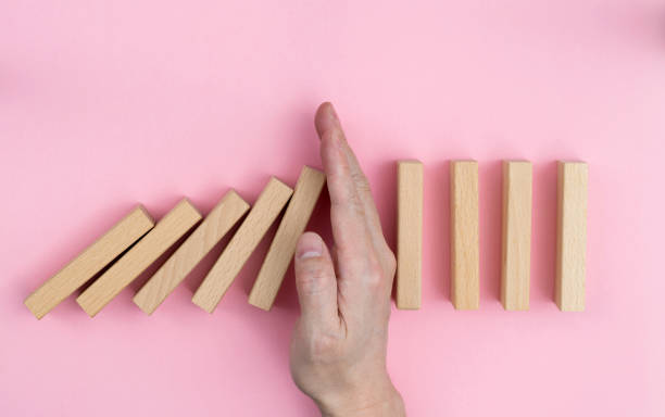 istock Man hand stopping the dominos falling 1607507170