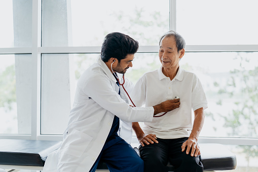 Image of an Asian Indian doctor examining senior man patient with a stethoscope in clinic