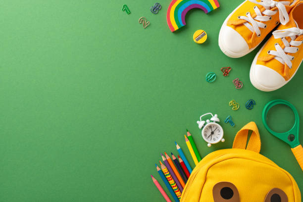 Schooltime essentials in focus: Top-view shot capturing a green blackboard setting adorned with delightful school stationery, a kid's school bag and shoes. Great for educational themes