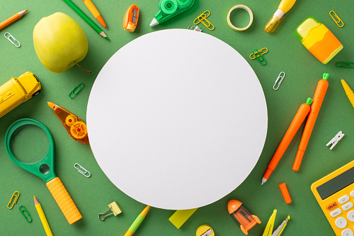 Unleash your imagination with top view learning essentials. From carrot-shaped pens to colorful pencils and apple, they're all here on green board background with empty circle for text or ad content