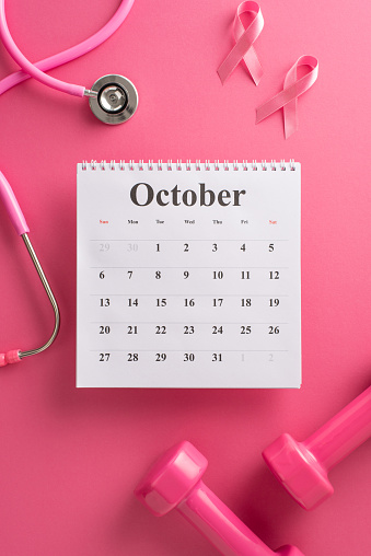 Advocating Breast Cancer Awareness Month. Bird's-eye top vertical view of a calendar, stethoscope, weights and pink ribbon on a bright pink isolated background, with copyspace for text or promotions