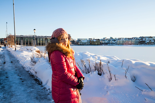 A young woman posing in Tjornin Lake view during winter which is a prominent small lake in central Reykjavik, the capital of Iceland