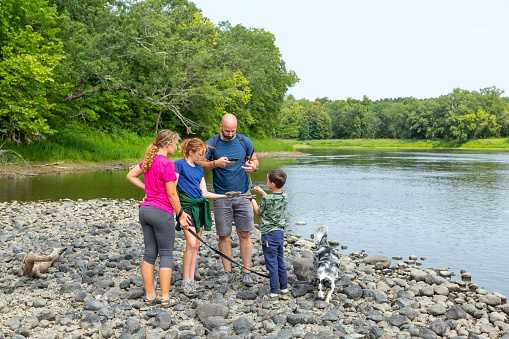 Family exploring the bed of the Mississippi River with their dog on a summer day. It has been a dry summer, and the river is very low. In this image the dad is taking a picture of the \