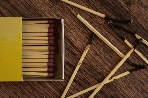A matchbox full of new match sticks inside and some burnt match sticks on top of a wooden table