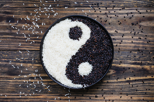 Nerone rice, organic forbidden black, and Jasmine Rice in a black bowl over wood background in Yin Yang shape. Table top flatlay view.