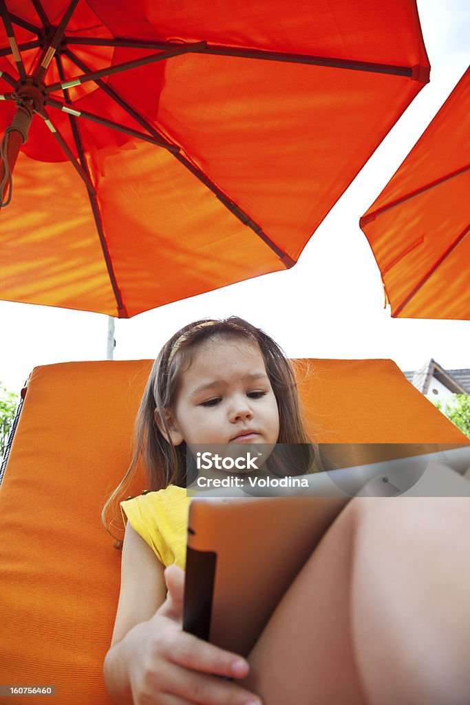 Сhild with tablet The child holds a tablet on a lounger on the beach under an umbrella Asian and Indian Ethnicities Stock Photo