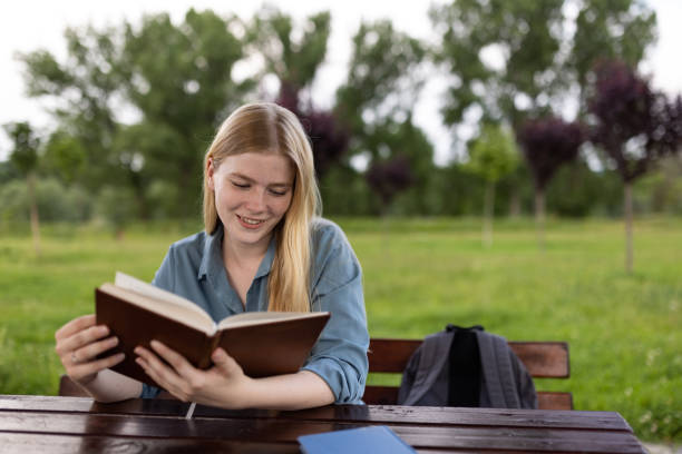 Beautiful woman reading a book while sitting on wooden bench in nature.