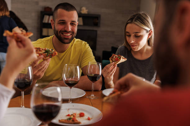istock Friends sitting at dining table, eating pizza and enjoying red wine 1607606780