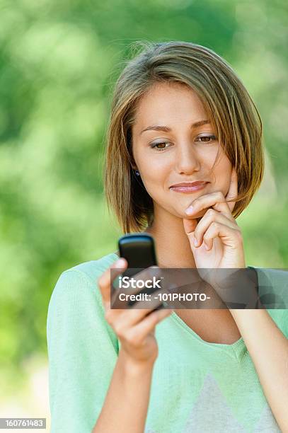 Mujer Joven Lee Sms A Un Teléfono Móvil Foto de stock y más banco de imágenes de Adulto - Adulto, Adulto joven, Aire libre