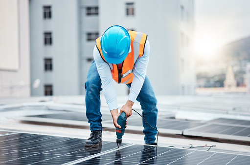 Engineer man, drill and solar panel on roof with industry, sustainability or construction in city. Technician, power tools and photovoltaic system for building, development or renewable energy in cbd