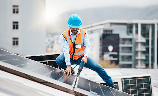 Technician man, drill and solar panel on roof with installation, sustainability and construction in city. Engineer, tools and photovoltaic system with building, development or renewable energy in cbd