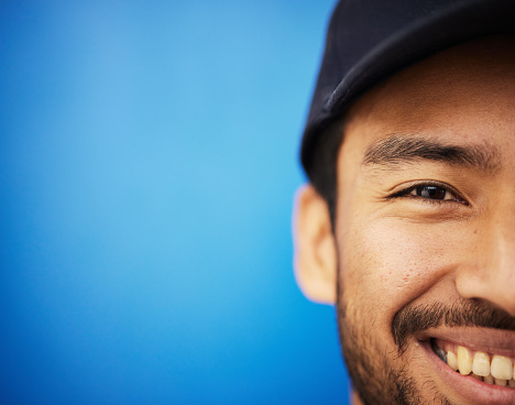 Studio, portrait and closeup on half of man in sports on blue background with advertising, mockup or space with athlete. Happy, face and smile with cricket or baseball cap and fitness or wellness