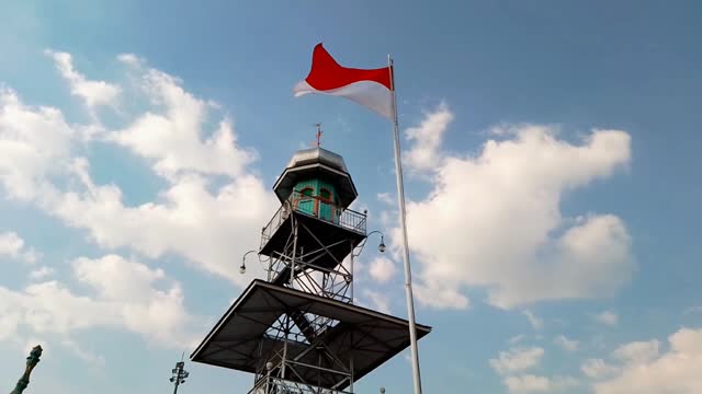 Demak, Central Java, Indonesia - 07-30-2023: Indonesia's flag is fluttering by wind with a wonderful blue sky background beside the tower of Agung Demak Mosque. Towards independence day of Indonesia.