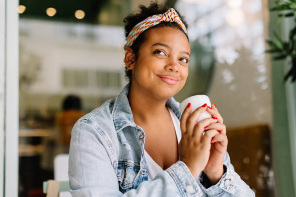 jeune femme dégustant une boisson chaude dans un café confortable - coffee shop coffee break coffee cup holding photos et images de collection