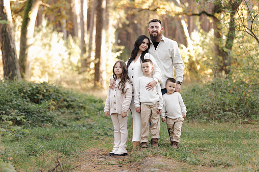 Portrait of big family outdoors. Young Stylish bearded dad with little son on shoulder, beautiful brunette mom, child boy and daughter in autumn park, smiling and looking at camera. Happy family day.