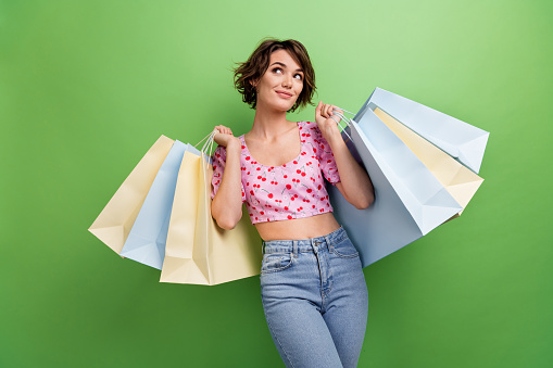 Photo portrait of attractive young woman empty space shopping bags wear trendy pink cherry print clothes isolated on green color background.