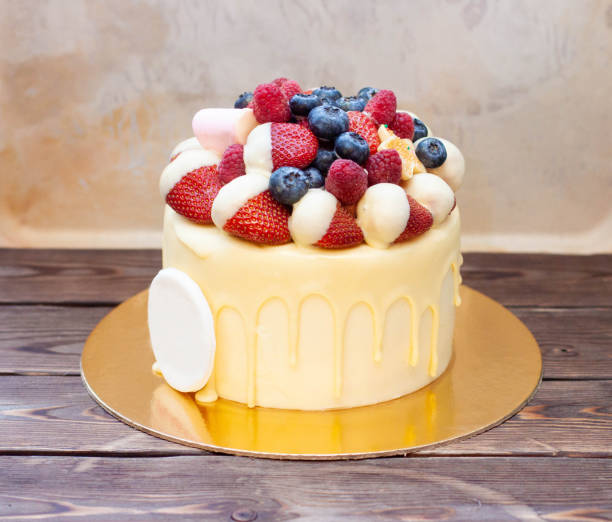 istock Yellow birthday cake with strawberries dipped into white chocolate, fresh raspberries and blueberries on vintage background 1607709113
