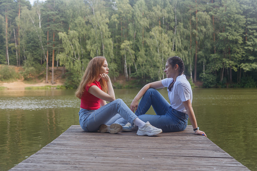 Two girls are sitting on a wooden bridge. Two friends are resting near the water. friendship, friends