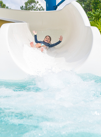 Happy little girl slides into a pool on a water slide