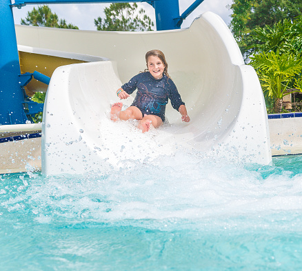 Happy little girl slides into a pool on a water slide