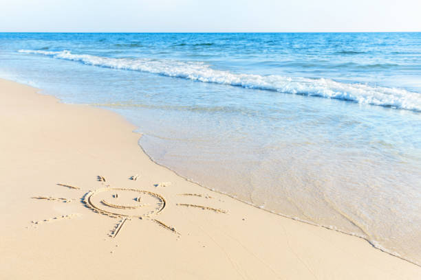 The sun symbol drawing on sand beach with soft waves
